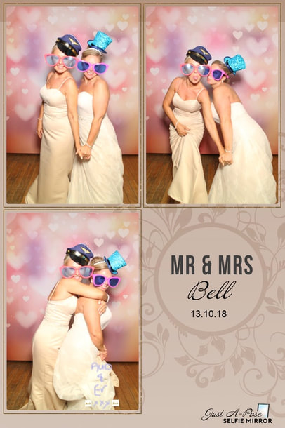 Two bridesmaids using selfie mirror photo booth with heart backdrop